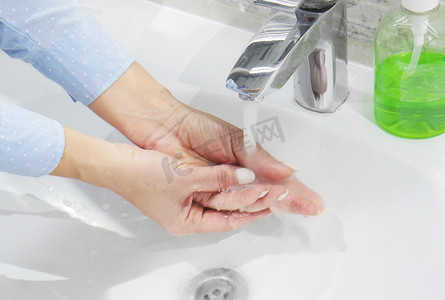 在洗脸盆的流水下用肥皂或凝胶洗手，清洁和卫生，女人的手穿着蓝色衬衫