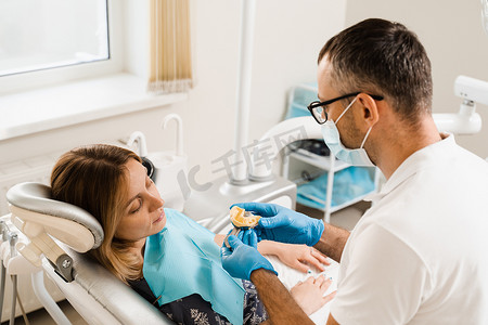 牙医在种植牙前展示患者妇女的牙齿模型。