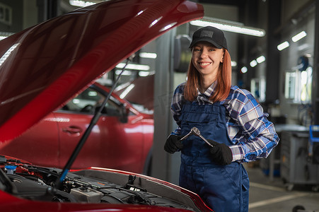 一名女汽车修理工站在汽车的引擎盖前，手里拿着一把螺丝刀。