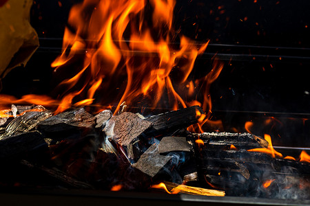 红色火焰燃烧摄影照片_烧烤炉坑，带有红色火焰、热木炭煤球和余烬的发光和燃烧的热明火