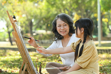 老人画画摄影照片_可爱的小女孩和祖母在夏日公园画画，一起在户外度过休闲周末