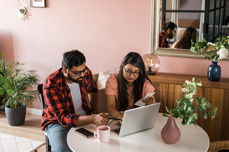 年轻的千禧一代印度丈夫和妻子做家庭文书工作、会计工作并审查纸质账单、笔记本电脑收据、使用在线计算器并在互联网上支付抵押贷款租金 — 经济危机概念
