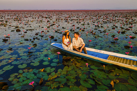 荷花开了摄影照片_一对夫妇在泰国乌隆他尼的红莲花海 Kumphawapi 的船上，那里开满了粉红色的花朵。