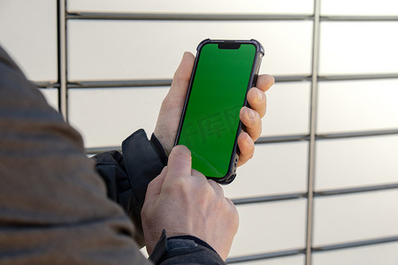 女性手持带有绿屏色度键的手机，位于包裹储物柜旁边，从购物储物柜收集包裹。