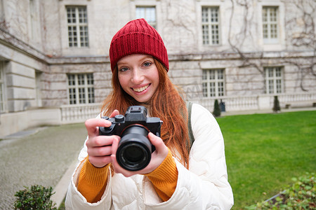 街头风格摄影照片_红发女摄影师在户外用专业相机拍照，捕捉街头风格的镜头，拍照时看起来很兴奋