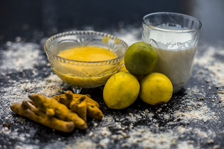 牛奶摄影照片_木质表面上的柠檬面膜，由柠檬汁、克粉或鹰嘴豆粉、姜黄或哈尔迪和牛奶组成，装在玻璃碗中。用于治疗晒黑。