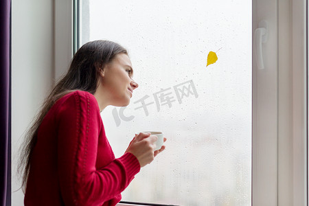 女人望着窗外雨滴、秋黄叶的肖像