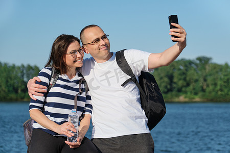成熟幸福的情侣在手机上自拍，人们在夏日傍晚公园的河边放松