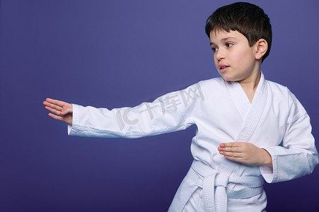 合气道摔跤手身穿白色和服的欧洲 10 岁男孩提高了他的战斗技能，隔离在紫色背景复制空间中。
