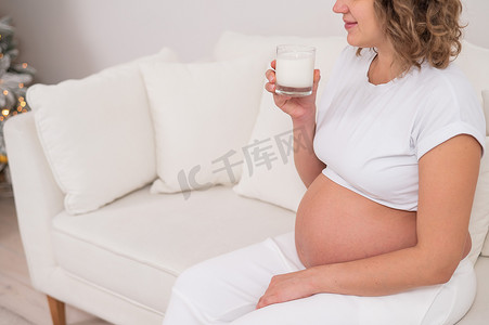 一名孕妇坐在白色沙发上喝牛奶。