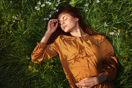 一个轻松的女人，躺在绿草丛中休息，穿着橙色长裙，闭着眼睛，脸上挂着愉快的微笑，正在康复