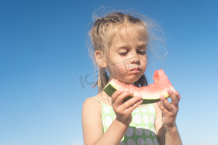 有趣的小女孩在阳光明媚的夏日在海滩吃西瓜。