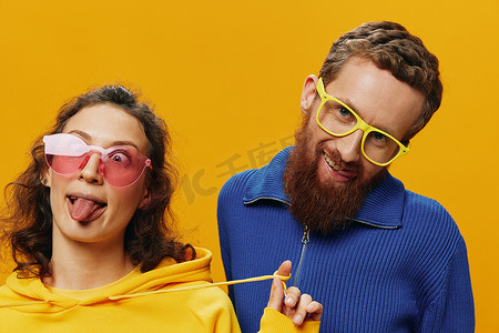广告黄色摄影照片_男女情侣欢快地微笑着，戴着眼镜，在黄色背景上，符号标志和手势，家庭拍摄，新婚夫妇。
