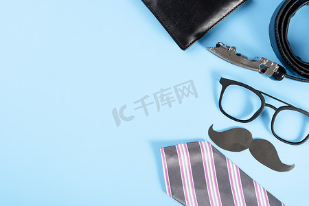 蓝色系网页模板摄影照片_父亲节快乐背景概念，蓝色背景上有粉色领带、眼镜、钱包、皮带和黑胡子，并有文本复制空间。