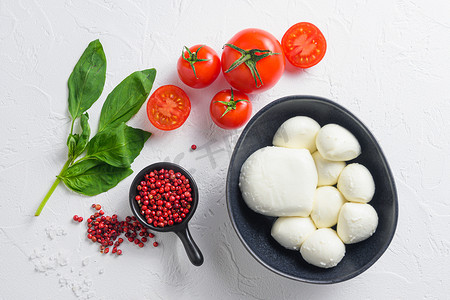 生熟的马苏里拉奶酪球，配有新鲜罗勒叶和樱桃番茄，配料，白色背景顶视图