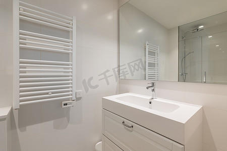 宽敞明亮的浴室配有内置于浴室梳妆台中的洗脸盆、一面反映房间另一侧淋浴的大镜子、天花板和用于烘干毛巾的暖气片。