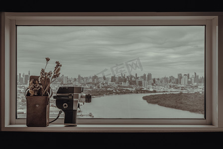 8 毫米老式电影摄影机和迷你棕色皮包中的干花，位于玻璃墙旁，可欣赏城市和河流景观。