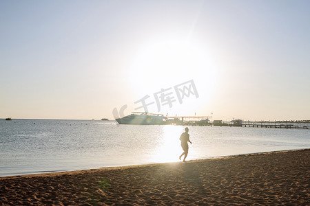 黎明时分，一个男人沿着海滩奔跑的剪影。