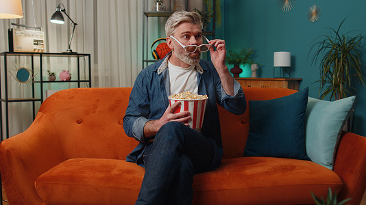 男人坐在沙发上吃爆米花，在家观看有趣的电视连续剧、在线体育比赛