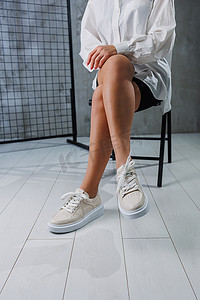 女性细长的双腿，穿着带鞋带的米色休闲运动鞋。