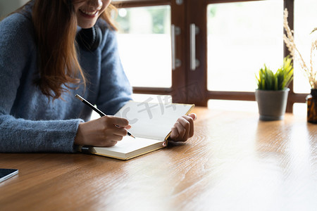 女性在笔记本电脑上远程在线学习的特写镜头在家里桌子上的笔记本上写下笔记。