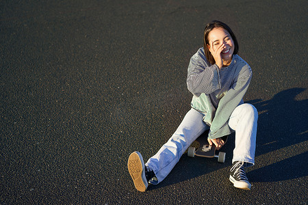 快乐美丽的韩国少女坐在滑板上，在长板上巡航，穿着休闲服