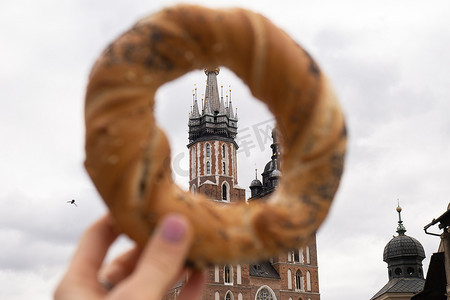 旅游妇女在克拉科夫主广场 Rynek Glowny 波兰的市场广场圣玛丽大教堂上吃百吉饼 obwarzanek 传统波兰美食小吃。