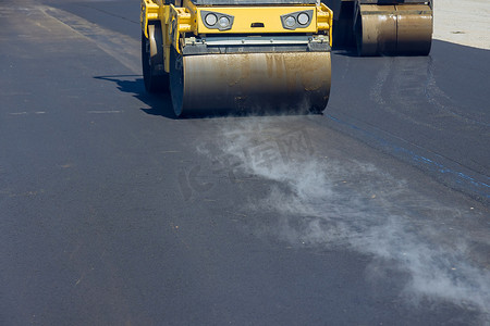 操作施工摄影照片_在振动压路机过程中，建筑工人正在操作在道路上铺设新沥青的机器
