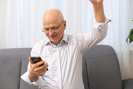 兴奋的老年成熟退休男子看着电话屏幕，庆祝在线彩票中奖或收到好消息。
