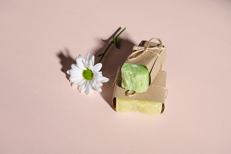 手工制作的生态友好肥皂条，含有天然成分和洋甘菊花，孤立的粉色柔和背景