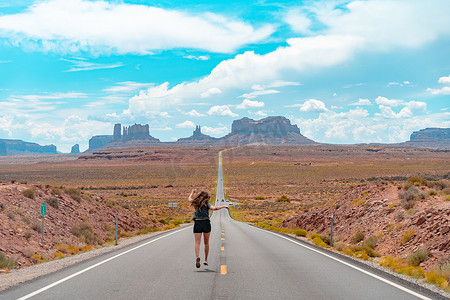 从后视来看，有魅力的年轻女子在沙漠中的美国直路中间奔跑。