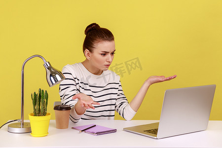 想要看的表情摄影照片_女人坐在工作场所，带着笔记本电脑，带着愤怒的表情看着笔记本电脑屏幕。