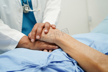 医生手牵亚洲老年女病人的手，在医院提供帮助和护理。