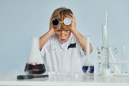 穿着外套的害怕的小男孩在实验室里用设备扮演科学家
