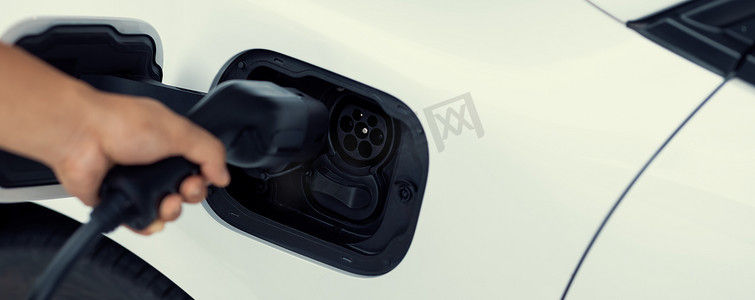 绿色充电汽车摄影照片_特写镜头焦点手插入电动汽车充电器到先进的电动可充电汽车。