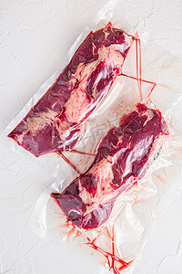 一对卡盘卷牛排，真空包装的有机肉，用于在白色混凝土纹理背景上进行真空烹调，顶视图。