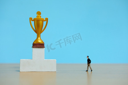 微型商业概念 — 商人走向白色讲台上的金色奖杯