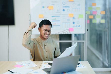 一位男性企业主在工作中使用计算机和财务预算文件成功投资自己的企业时露出幸福的笑脸的肖像