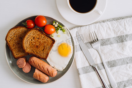 早餐盘，配有一杯黑咖啡、烤香肠和全麦吐司，盘子上配有煎鸡蛋和樱桃番茄