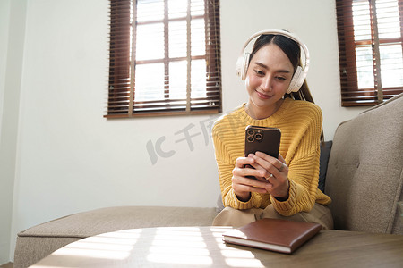 微笑的女孩在家里放松，她正在用智能手机播放音乐，戴着白色耳机
