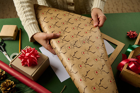 赛事时间摄影照片_细节：女人的手在包装圣诞礼物时铺开带有鹿图案的包装纸。