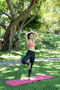 运动健身垫摄影照片_年轻漂亮的女孩正在公园中央的健身垫上做高级瑜伽体式。