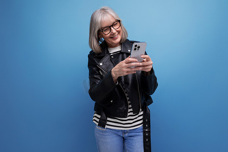 精力充沛的 60 年代现代中年女性，头发灰白，在明亮的背景下使用智能手机在互联网上聊天