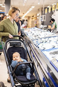 婴儿推车摄影照片_穿着休闲装的母亲带着婴儿推车在超市杂货店的鱼市场部门挑选鱼。