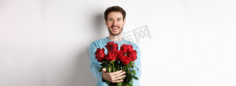 留着胡子的帅哥伸出双手，送出玫瑰花束，微笑着，在浪漫的约会中带来鲜花，与情人一起庆祝情人节，站在白色背景上