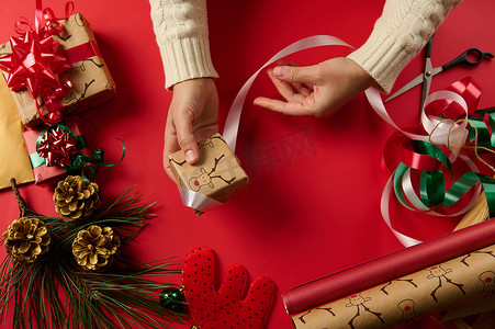 圣诞快乐小鹿摄影照片_正上方，女人的手用鹿图案的礼品纸包裹一份小礼物，用白丝带绑起来