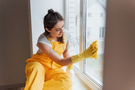 穿着黄色制服清洁窗户的家庭主妇。