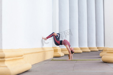 苗条迷人的运动女运动员在户外练习瑜伽，做墙辅助倒立姿势。
