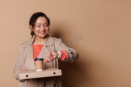 扁平女扁平摄影照片_女人检查手表上的时间，把披萨放在纸板扁盒里，把外卖咖啡放在纸杯里。