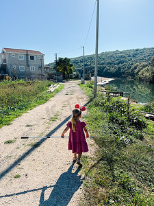 儿童米米摄影照片_头戴米妮耳朵、手里拿着登陆网的小女孩沿着河岸行走